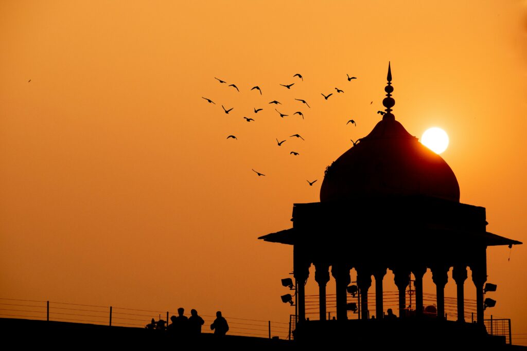 Silhouette view of Humayun's Tomb in Delhi at sunset, featuring birds in flight and rich orange hues.
