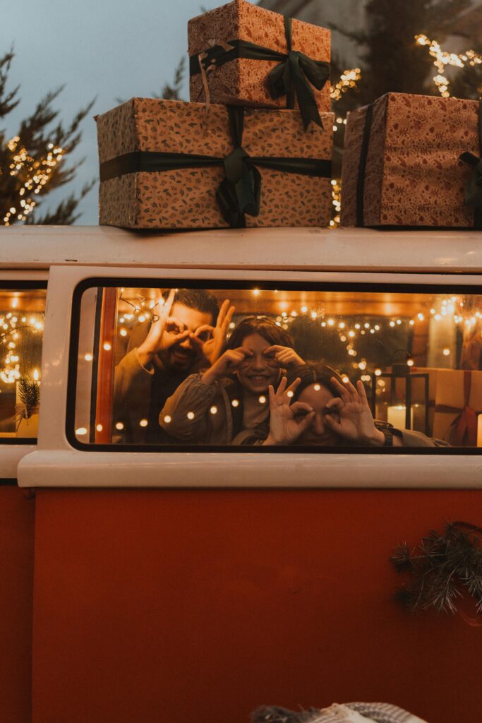 A group celebrating the holiday season inside a van with festive lights and gift boxes on top.
