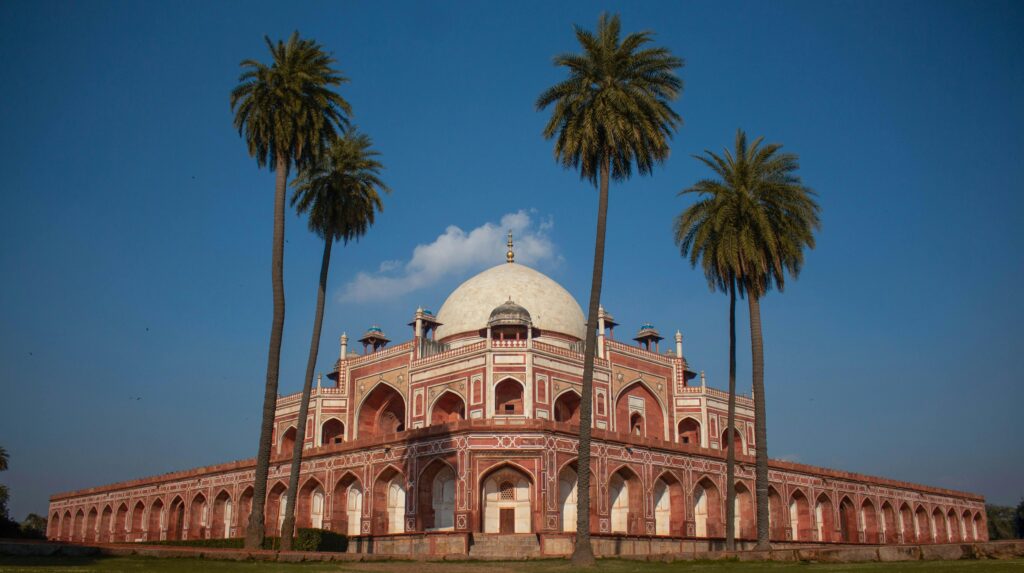 View of Humayun's Tomb, a UNESCO World Heritage site in Delhi, India, with palm trees and blue sky.